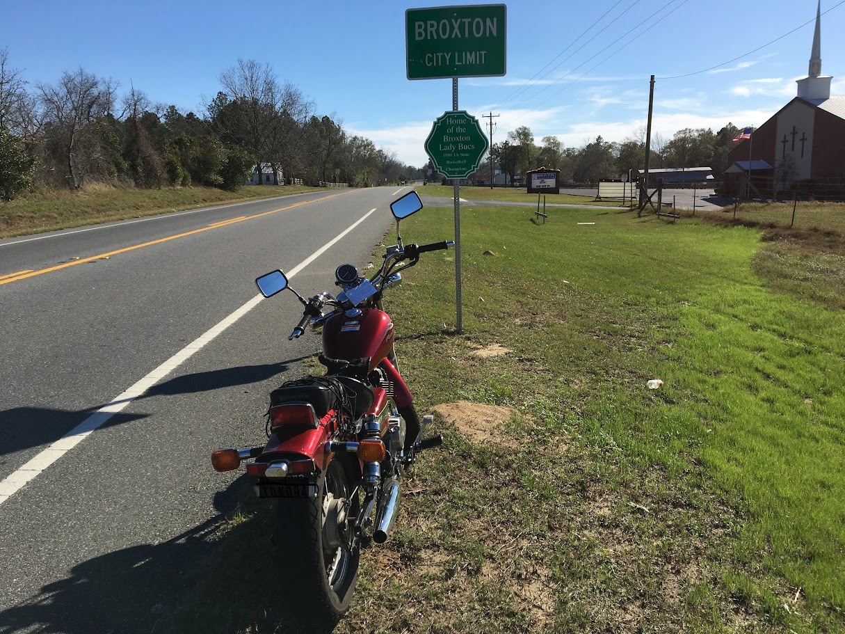 Candy Red 2012 Honda Rebel motorcycle parked in front of road sign entering Broxton, Georgia in December 2016